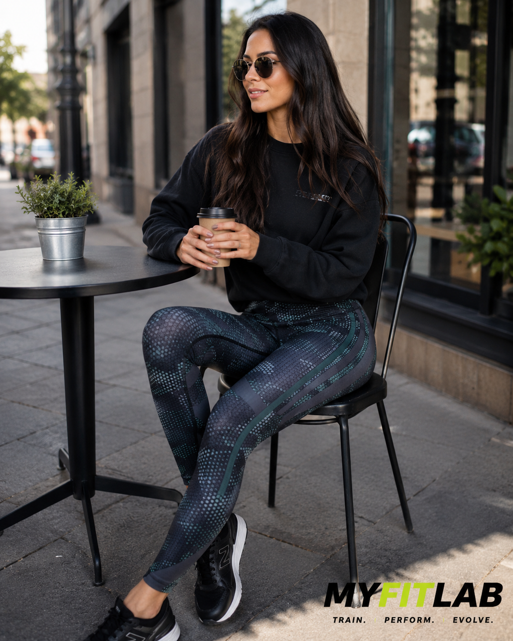 Woman wearing Carbon Edge Leggings with flowing gray/black and green design while having coffee on a patio